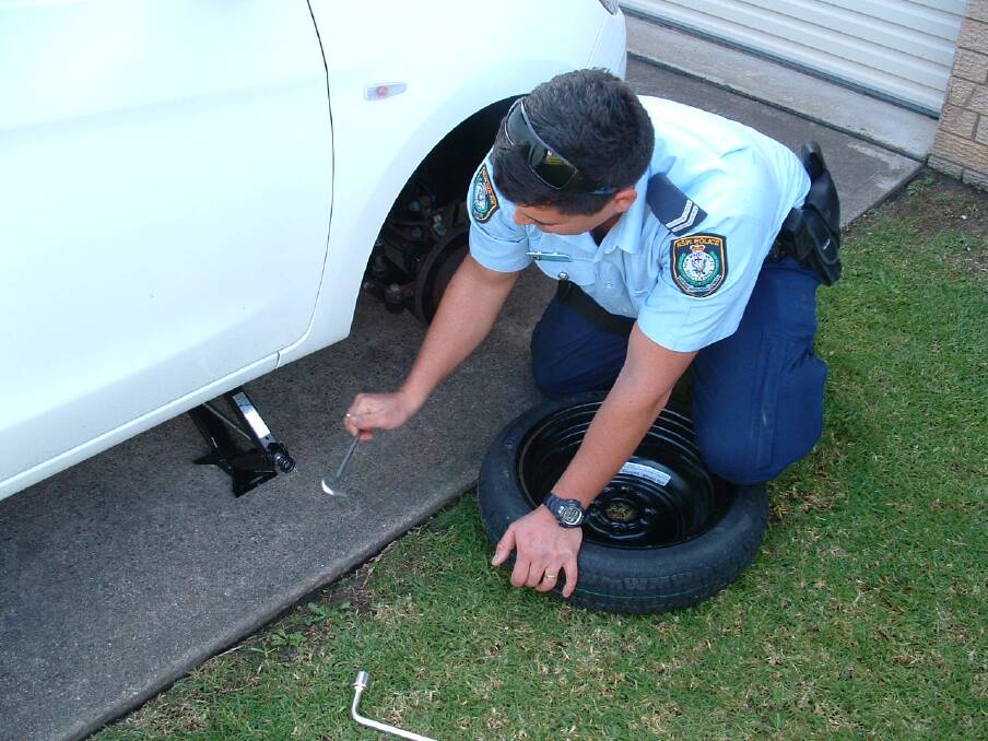 Senior Constable Gavin Warner of the Narooma police goes beyond the call of duty in installing the car’s spare wheel after a thief made off with one of the car's wheels. 