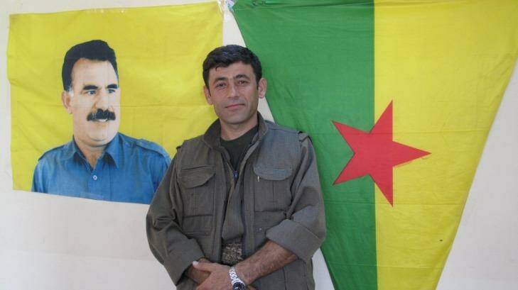 Commander Badr Khan standing under a flag featuring the image of Abdullah Ocalan, the imprisoned PKK leader. Photo: Ruth Pollard