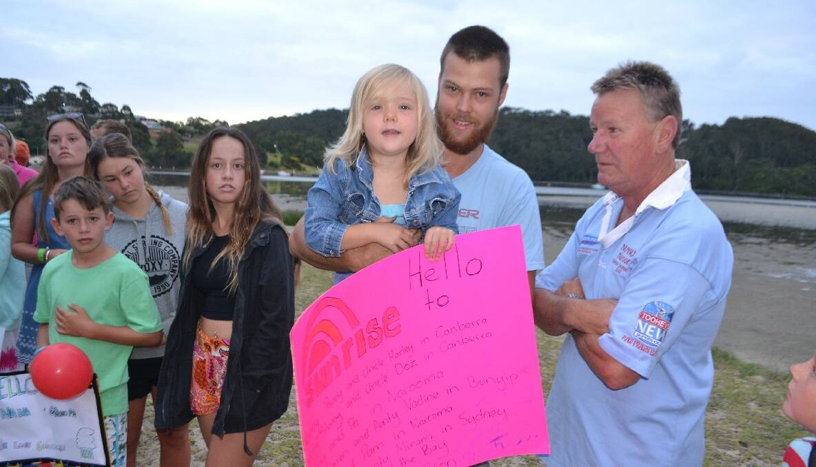 HELLO SUNRISE: Narooma local Rowan Hawkey and his daughter Alexis, 4, with their sign saying hello to all their relatives around Australia and Numnut Brent Lockton. 