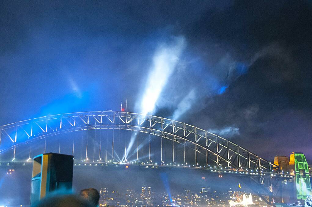 FLEET FIREWORKS: Fireworks launched from forecastle of HMAS Sydney while “Search Lights” shine down from the bridge - one of many sights where search lights were projected into the night sky. 