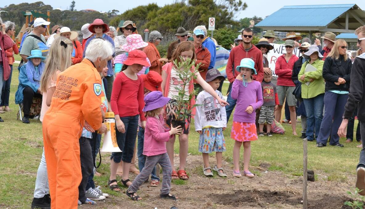 TREE PLANTING: One of the event organisers Patricia DeLaney in her orange jumpsuit helps children who volunteered to plant three trees at the park at Bar Beach. 