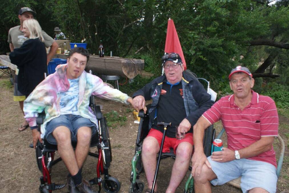 RAY’S CHAIR: Jordan Willis, Ray Hirst in his new wheelchair and Trevor Bennett sitting by the campfire on the banks of the Tuross River.