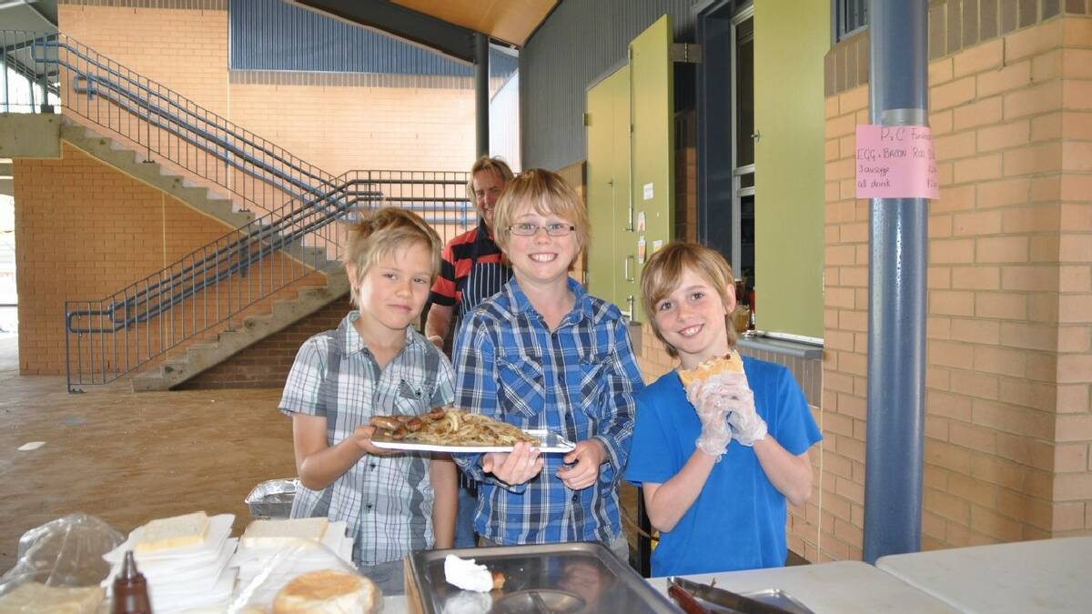 Don Peterson in the background manning the barbecue at Merimbula Public School with help from Jacob Shields, left, and Mackenzie and Edward Peterson.