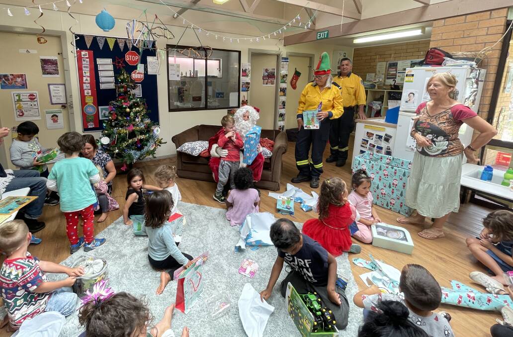 Little Yuin Preschool director Kim Cooke (standing, right) watched as Tilba RFS helped Santa Claus distribute the presents. Picture by Marion Williams