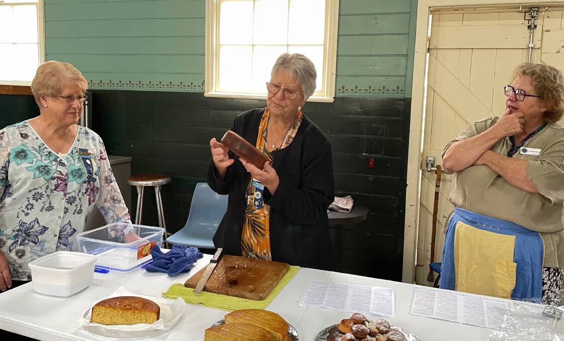 CWA Far South Coast Group Land Cookery Officer Liz Tough (left) and Tilba branch vice-president Annette Kennewell (right) watch as experienced Land Cookery judge Barb Smith (centre) assesses a gluten-free whole orange cake. Picture by Marion Williams.