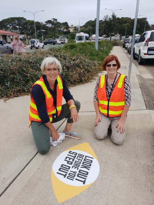 LOOK OUT: Eurobodalla Shire Council's Yvonne Hutcheson and Kate McDougall install a 'Look out before you step out' sticker in Narooma to highlight pedestrian safety.