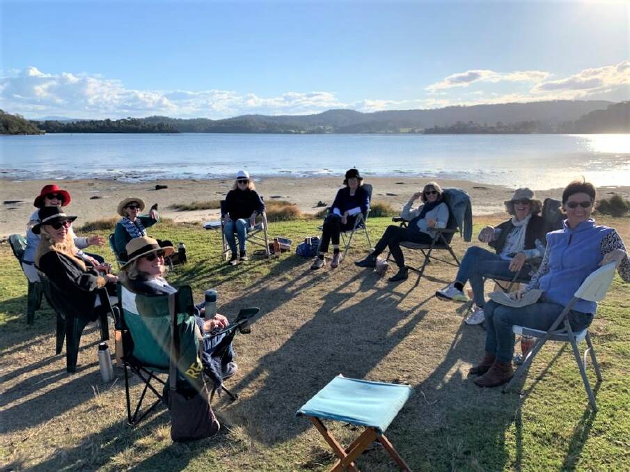Bonding over books: Women of Narooma Bookclub perched up on parkland to discuss their latest read. Image: Supplied. 