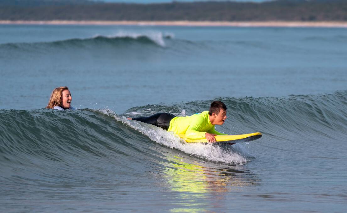 Occupational therapist Gabbie Johnson pushed client Lochie Nielson onto a wave at Broulee recently. Picture: Josh Burkinshaw. 