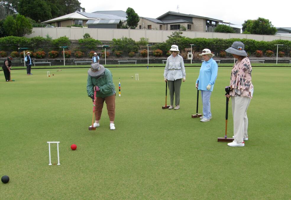 Club Captain Christine Stent, on the march in golf croquet, plays the red ball to hoop 6 in game 1, watched by partner Louise Starkie and opponents Pearl Hanson and Cathy Sforcina