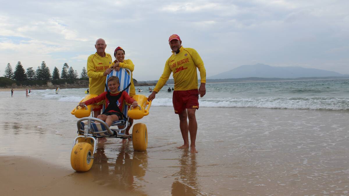 ALL IN: Bermagui SLSC president Bruce McAslan, secretary Cheryl McCarthy and captin Andrew Curven test the new wheelchair with Zane Curven.