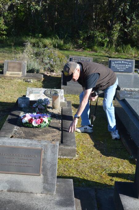 Narooma RSL sub branch member, Ian Noormets-Booth exams the weatherworn grave of a war veteran at Narooma Cemetery.