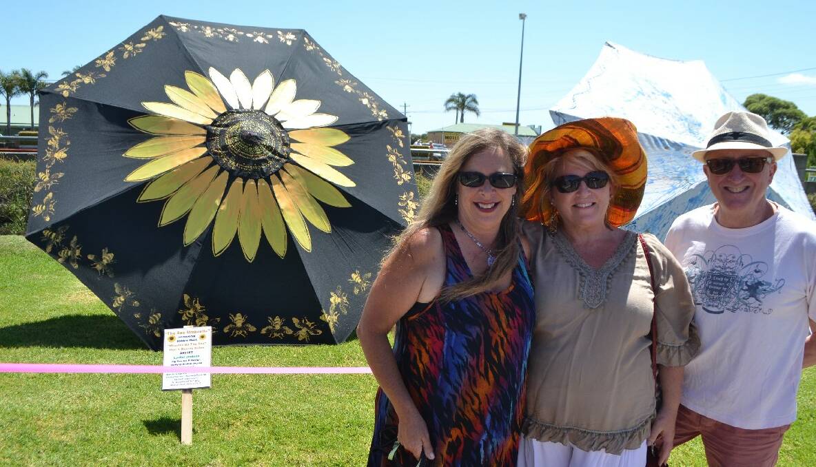 ARTIST AND SPONSORS: Local Bermagui artist Lyndal Jenkins with her bee inspired umbrella and its sponsors Robbie and Garry Hart of “Miracles by the Sea” beauty salon. 